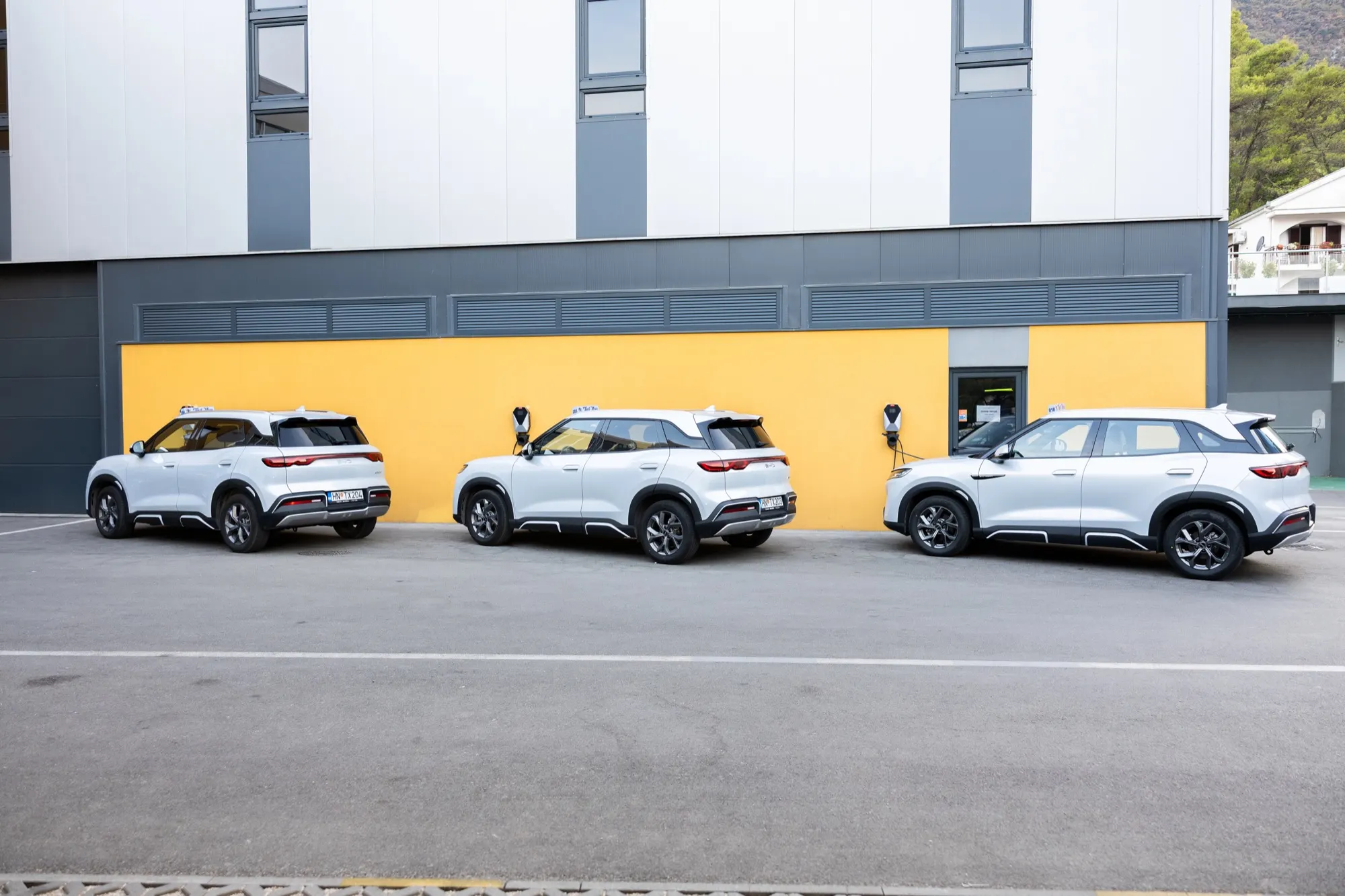 Tri BYD taksija na punjenju ispred žutog zida